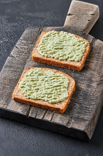 Sandwich of whole grain bread and guacamole on an old wooden board.