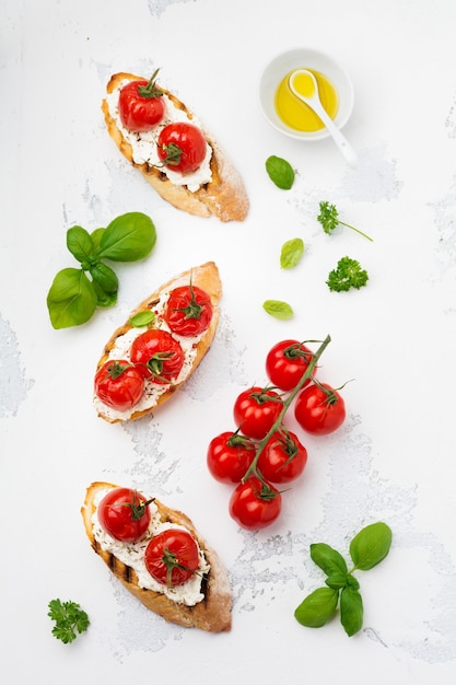 Sandwich with baked cherry tomatoes, garlic, olive oil and curd cheese on white surface