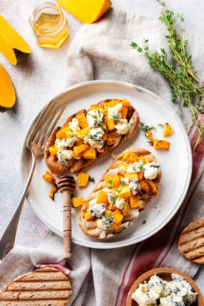 Sandwich with baked pumpkin and dorblu cheese with blue mold, honey and thyme on a concrete old light background. Top view