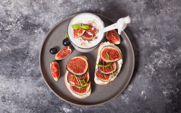 Sandwich with cream cheese, figs and honey and yogurt in a glass served on the gray plate on the concrete . Healthy food .