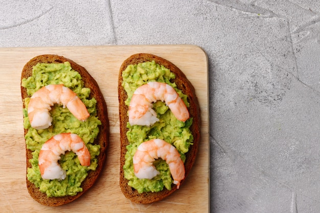 Sandwich with guacamole and shrimp on cement background