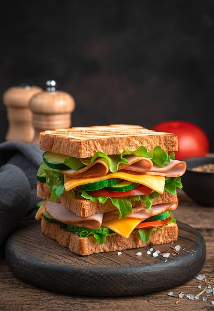 Sandwich with ham, cheese, tomatoes and cucumbers on a brown background. Side view, close-up