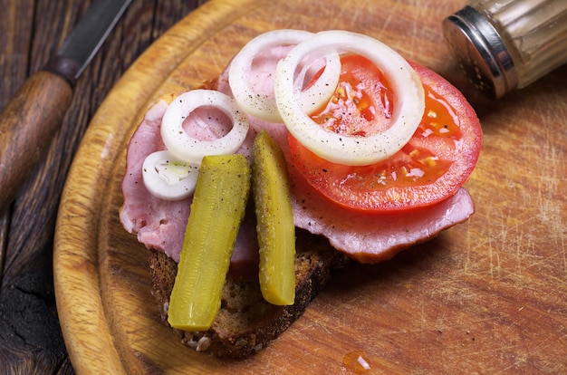 Sandwich with ham, onions, tomatoes and cucumbers on rustic table