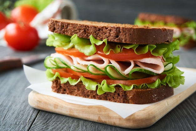 Sandwich with ham, tomato, cucumber and lettuce on a wooden cutting board