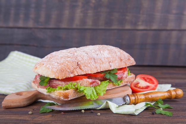 Sandwich with ham and vegetables on a dark wooden background.