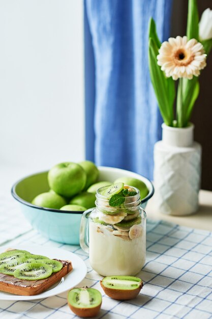 Sandwich with peanut butter and kiwi, green apples, yogurt with banana and kiwi, creative idea for kids breakfast, dessert or holiday meal, top view flat lay, healthy food for children. Good morning