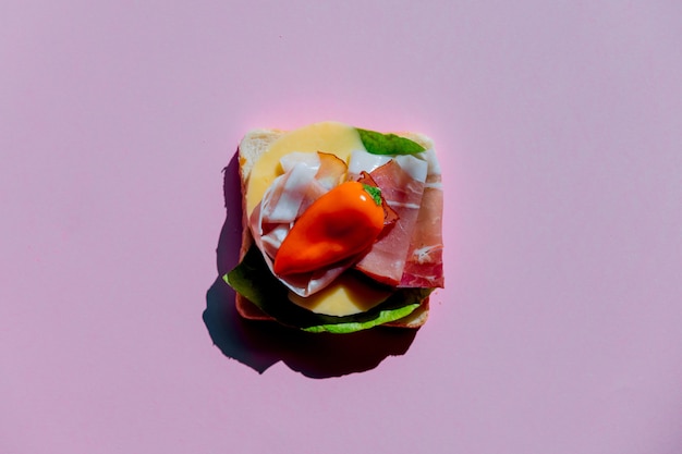 Sandwich with pepper, ham and cheese on purple background. Above view