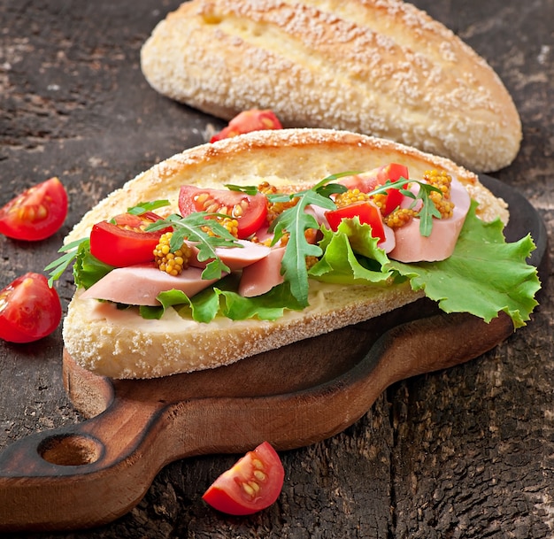 Photo sandwich with sausage, lettuce, tomato and arugula on the old wooden background