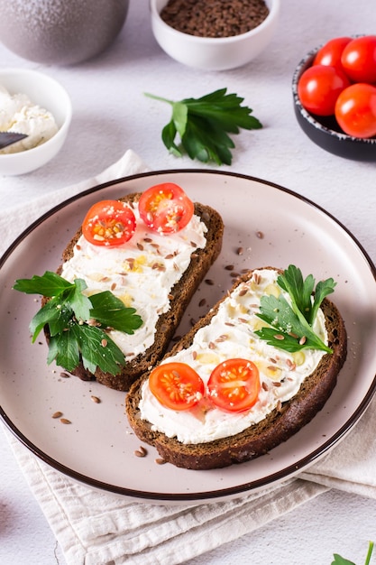 Sandwiches on rye bread with ricotta tomatoes and parsley on a plate on the table Vertical view