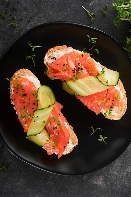 Sandwiches Salmon toast with cream cheese cucumber black sesame and microgreens on black background Seafood Healthy food Photography in low key Top view