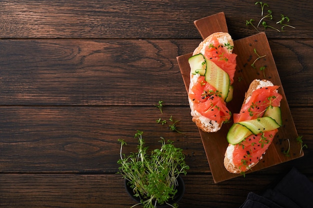 Sandwiches Salmon toast with cream cheese cucumber black sesame and microgreens on old wooden table background Seafood Healthy food Photography in low key Top view