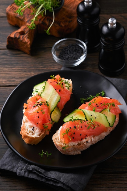 Sandwiches Salmon toast with cream cheese cucumber black sesame and microgreens on old wooden table background Seafood Healthy food Photography in low key Top view