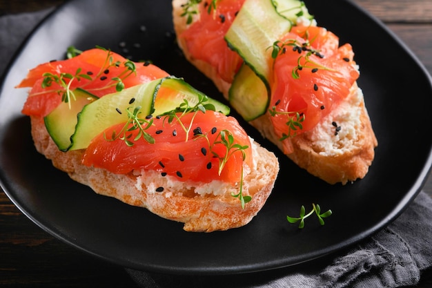 Sandwiches Salmon toast with cream cheese cucumber black sesame and microgreens on old wooden table background Seafood Healthy food Photography in low key Top view