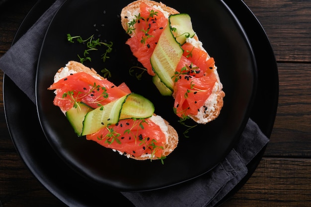 Sandwiches Salmon toast with cream cheese cucumber black sesame and microgreens on old wooden table background Seafood Healthy food Photography in low key Top view