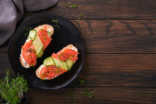 Sandwiches Salmon toast with cream cheese cucumber black sesame and microgreens on old wooden table background Seafood Healthy food Photography in low key Top view