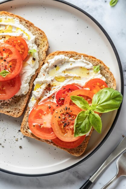 Sandwiches or toasts with tomatoes cream cheese olive oil and basil on white marble background