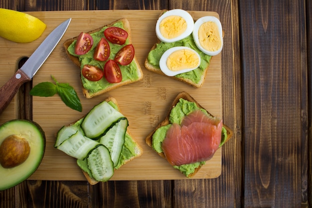 Sandwiches with avocado and different ingredients on the brown  wooden background.Top view.Copy space.