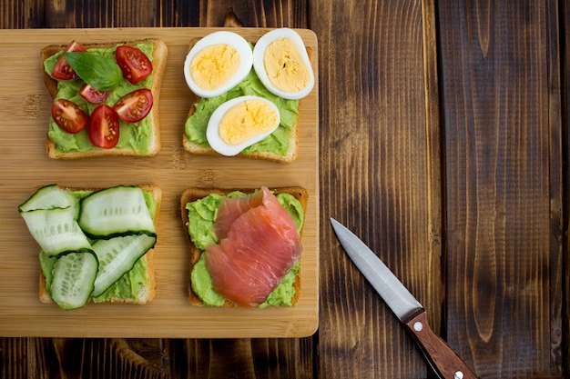 Sandwiches with avocado and different ingredients on the brown  wooden background.Top view.Copy space.