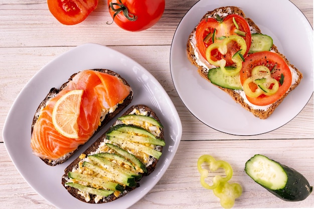 Sandwiches with cheese, salted trout, tomato, cucumber on a white wooden background