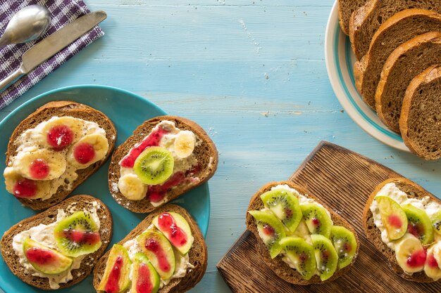 sandwiches with fruit cream banana apple and kiwi on a blue wooden background