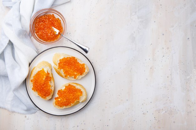 Sandwiches with red caviar and butter in plate on wooden table. Top view