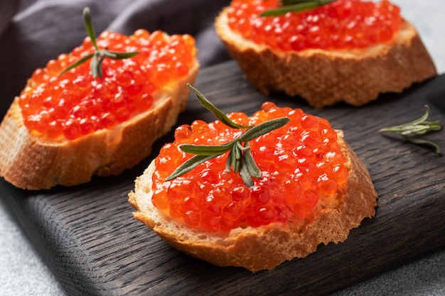 Sandwiches with red caviar on a white baguette with cottage cheese and rosemary.