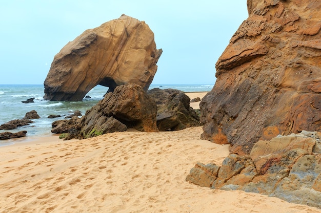 Sandy beach Praia de Santa Cruz with rock formation (Portugal). Misty weather.