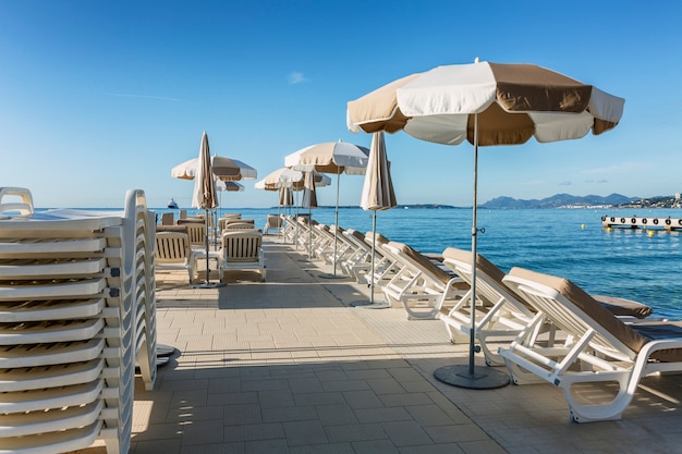 Sandy beach with empty sunbeds on the pier on a sunny day at the resort. French Riviera. Tourism and travel.