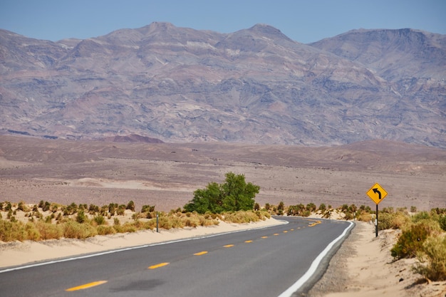 Sandy desert road leading into mountains in Death Valley