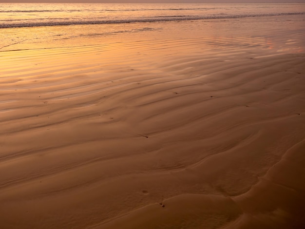 Sandy pattern and curved texture on the beach created by waves and sea breezes on sunset Wet sand beach with peace sea water background for summer holiday and tropical travel vacation concepts