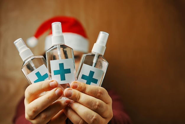 Sanitizers with turquoise cross on label in hands man in red santa hat christmas in quarantine new y...