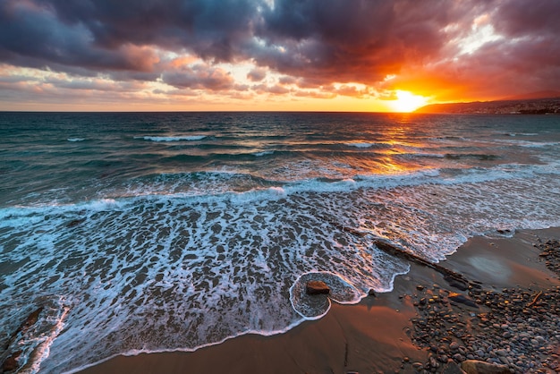 Sanremo Riviera dei Fiori Liguria Italy Scenis rocks and pebbles on beach illuminated beautiful by sunset light Dramatic colourful sky waving sea