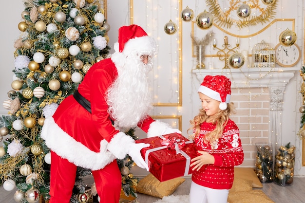 Santa Claus gives a baby girl a gift at the Christmas tree