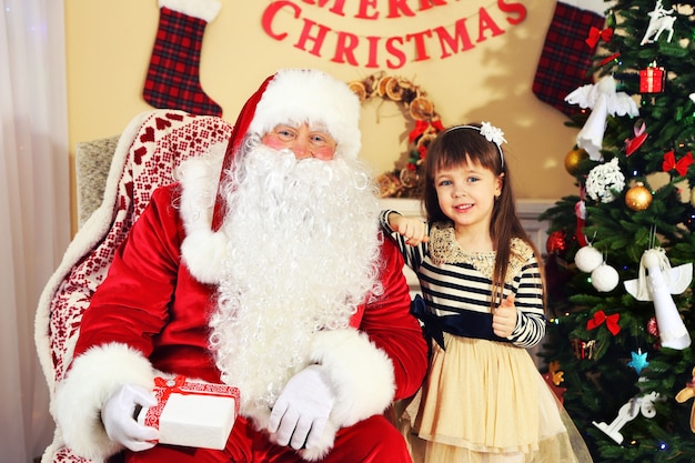 Santa Claus giving  present to  little cute girl near Christmas tree at home