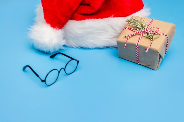 A Santa Claus hat a Christmas gift tied with string and round glasses on a blue background A postcard for the new year Copy space