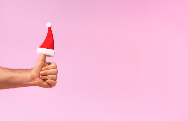 Santa Claus hat is put on the finger Hand is holding thumbs up Creative Christmas idea Copy space