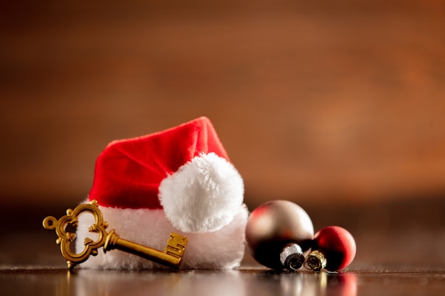 Santa Claus hat and key with baubles on wooden table