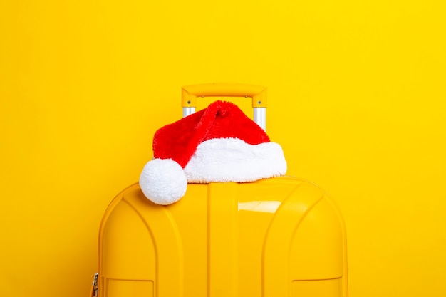 Photo santa claus hat lies on a yellow suitcase on a yellow background.