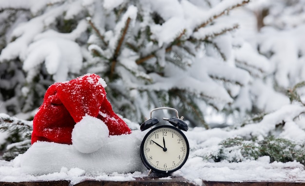 Santa Claus hat and vintage alarm clock in wooden table in blizzard