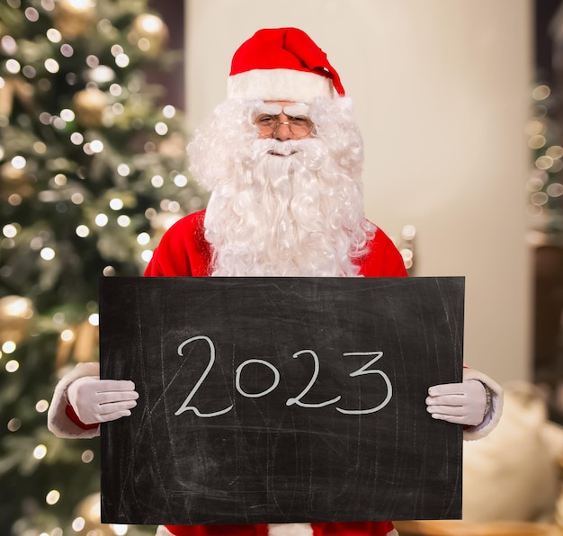 Santa Claus holding a blackboard with 2023 text