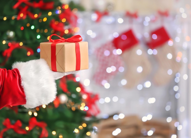 Santa Claus holding gift box against blurred Christmas lights