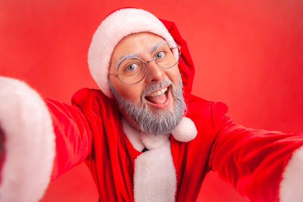 Photo santa claus making selfie pov, looking at camera with smile and positive expression.