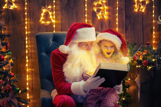 Santa Claus open and read magic book with little cute amazed girl in pajama