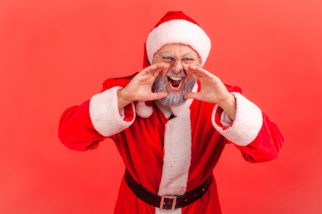 Photo santa claus screaming with angry facial expression, keeping hands near mouth.