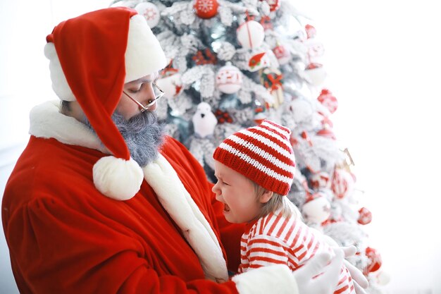 Santa Claus sitting with little cute elves over Christmas background Time of miracles Gifts from Santa Claus