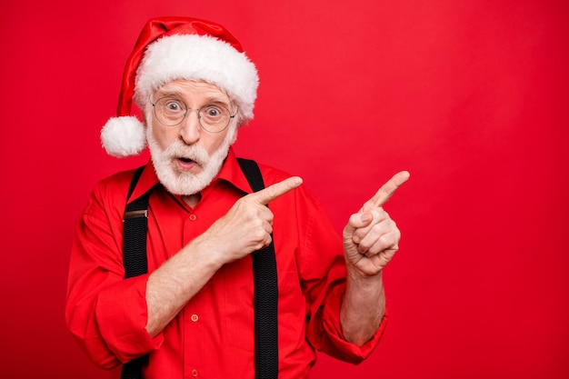 Photo santa claus in suspenders and hat posing on red wall