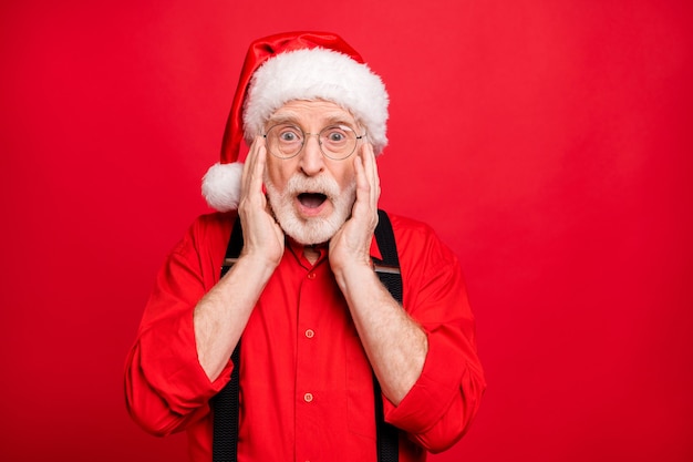 Santa Claus in suspenders and hat posing on red wall