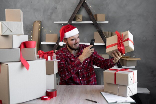 Photo santa claus takes pictures on a mobile phone camera while sitting in the office with boxes of gifts for christmas or goods from an online store