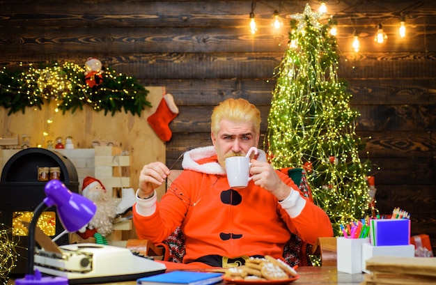 Santa claus with mug of milk and cookie sitting at table christmas background