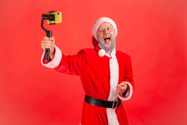 Santa claus with steadicam in hands, livestream, looking at phone screen and screaming.